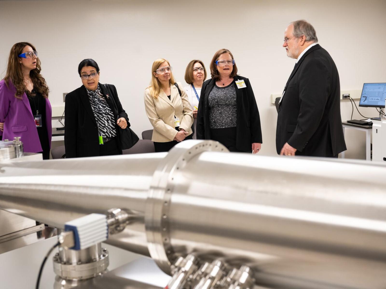 Six people standing near a mass spectrometer inside a facility building.