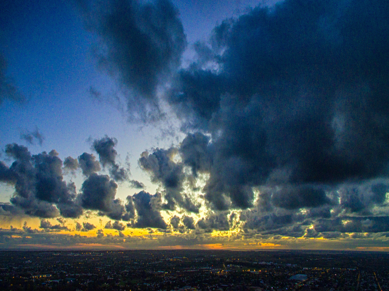 Photograph of clouds above an urban environment at sunset, with a dark blue sky.
